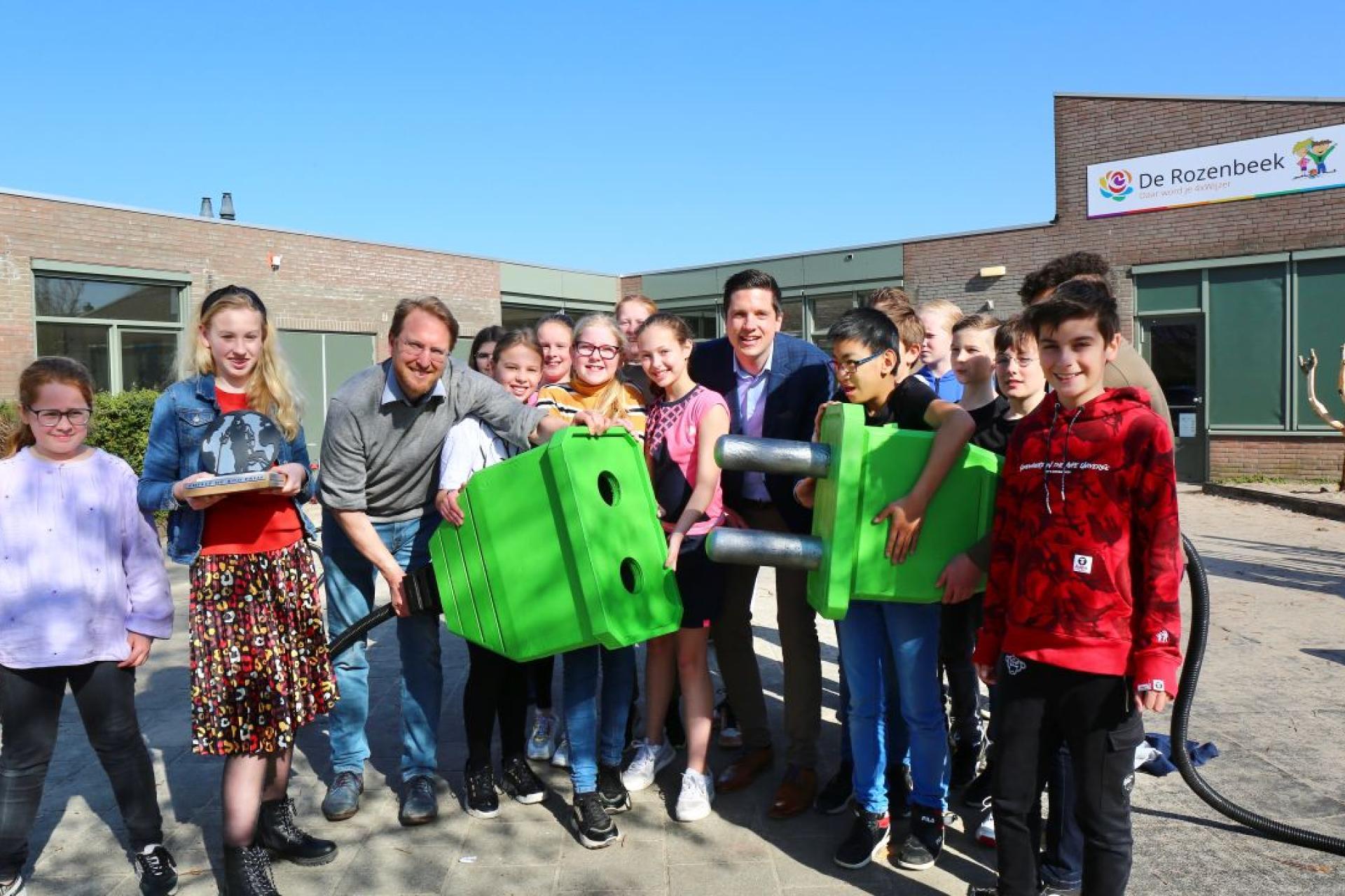 Wethouder Sebastian Dinjens poseert samen met kinderen van basisschool De Rozenbeek met een grote groene stekker