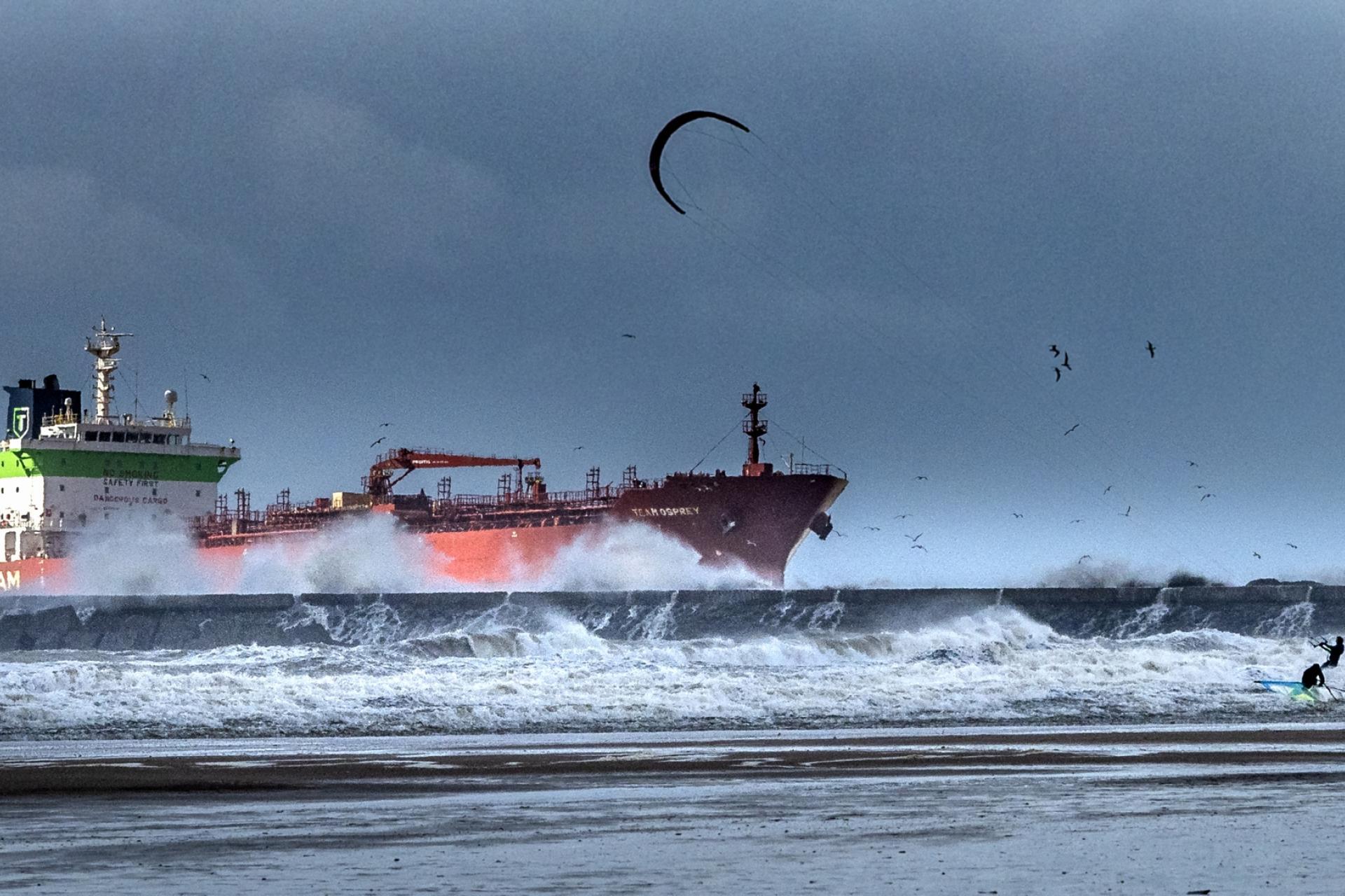Storm bij de pier van IJmuiden: een kitesurfer en een schip vechten met de golven